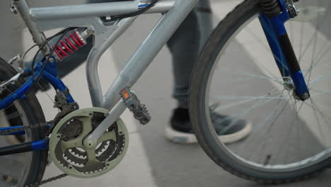 primer plano de la cadena de la bicicleta y el pedal como una persona en pantalones grises, zapatillas negras camina a su lado a través de un cruce de peatones pintado de color blanco