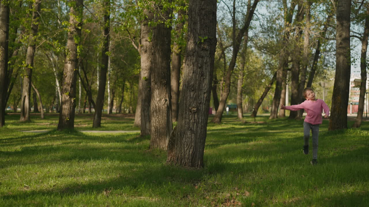 Cheerful little girl jumps around large tree in spring park