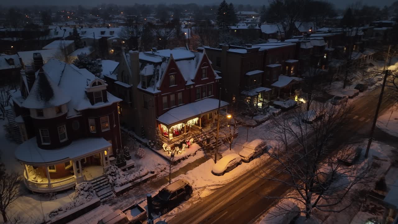Decorated house lighting at night during snowy winter day. Christmas time in charming small town of USA. Aerial top down descending shot.