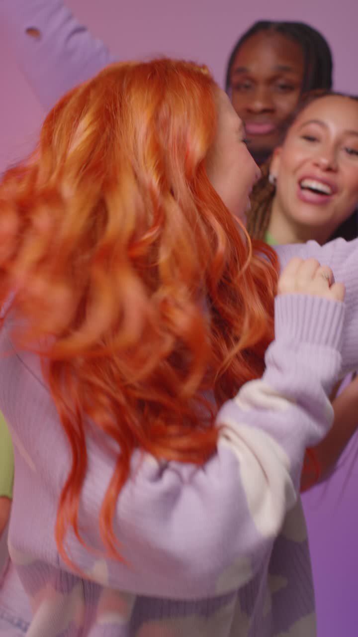 una toma de estudio de video vertical de amigos de la generación z bailando y posando para selfies en una fiesta contra un fondo rosa