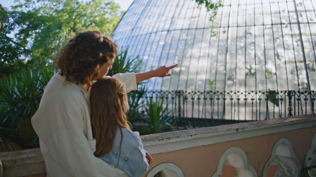 Mother showing daughter greenhouse at park looking distance embracing back view