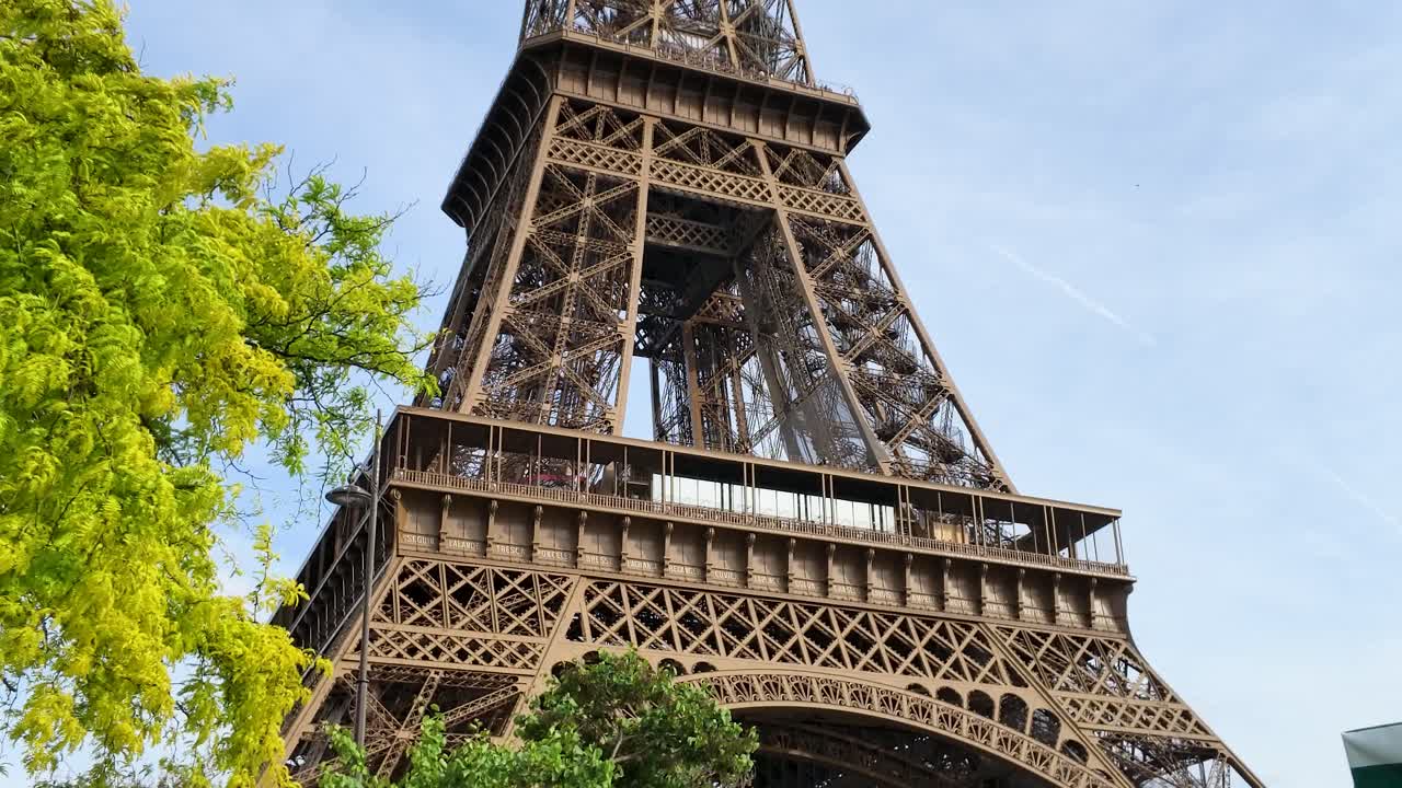 Una panoramica verticale verso il basso rivela la Torre Eiffel sopra bancarelle verdi del mercato e turisti indaffarati.
