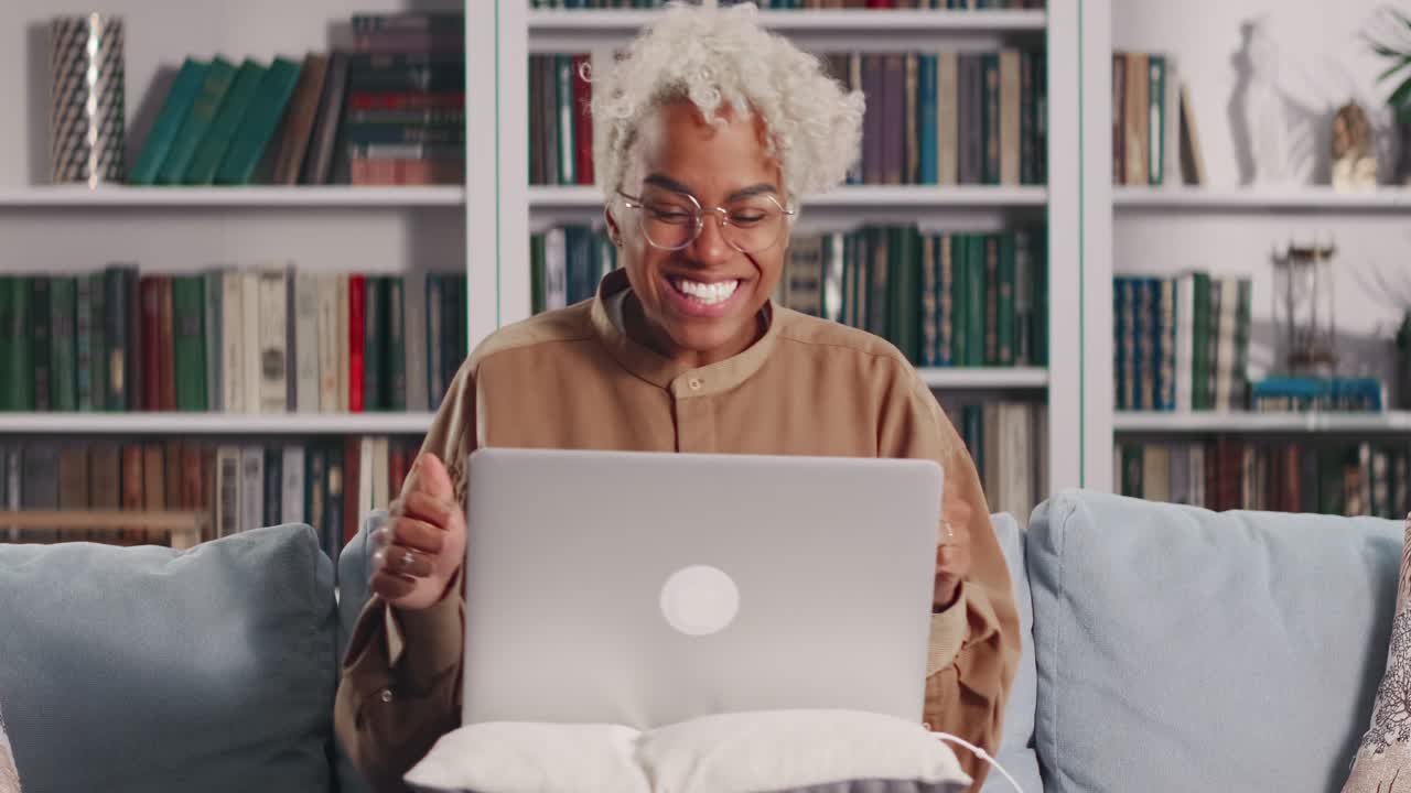 Giovane donna afroamericana con un laptop sulle gambe, felicissima per la notizia, seduta sul divano