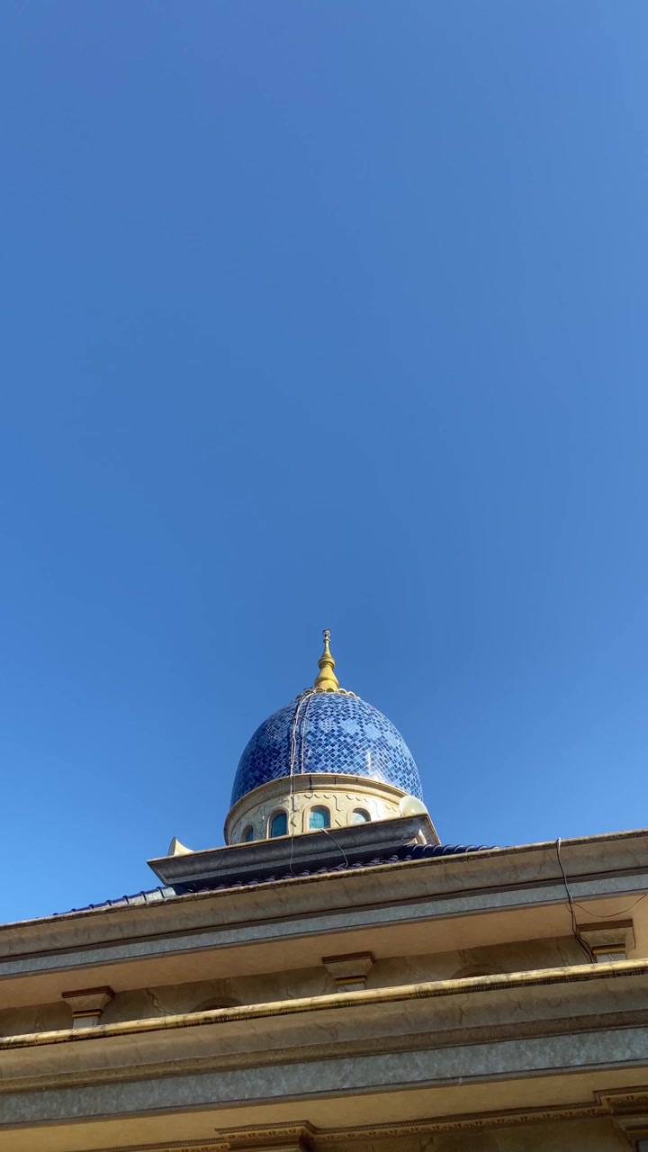 Cupola blu piastrellata e ornata con pinnacolo dorato contro un cielo azzurro limpido