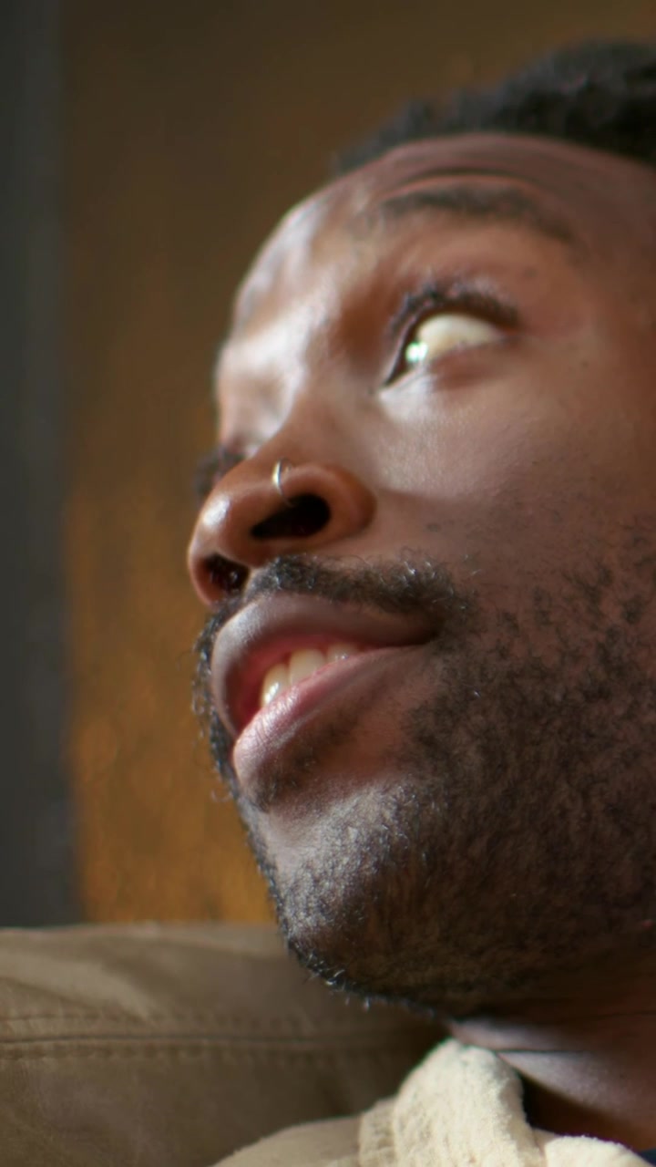 Vertical video: Hearing cue, Black man turning head on couch with nose ring and knit jacket