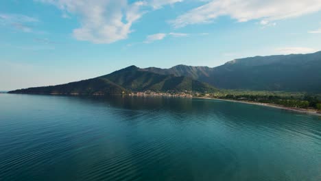 Aerial-View-Of-Golden-Beach-At-Sunset-With-Sun-Rays-Bursting-Through-Towering-Mountain-Peaks,-Beautiful-Beachfront-And-Lush-Green-Vegetation,-Vivid-Colors,-Thassos-Island,-Greece,-Europe