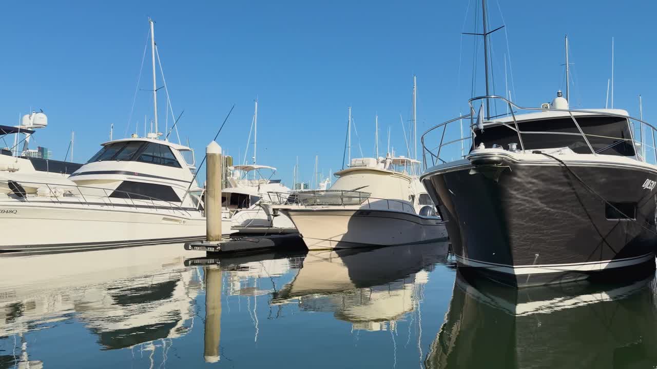 Una ripresa fluida con panning cattura yacht di lusso che si riflettono sull'acqua calma sotto un cielo azzurro limpido