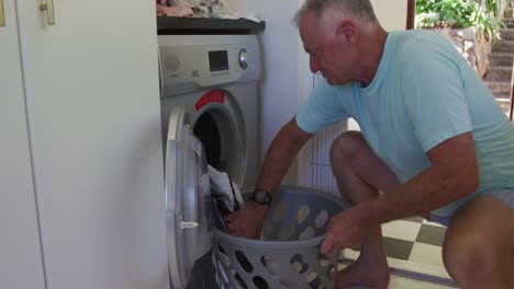 hombre mayor caucásico poniendo ropa en la lavadora en casa