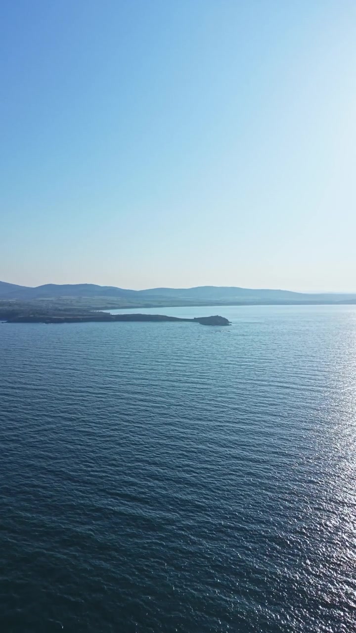 Meerblick mit ruhigem Wasser und fernen Hügeln tagsüber nahe der Küste, der blauen Himmel und natürliche Landschaft zeigt.