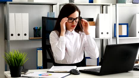 mujer de negocios quitándose las gafas y mirando a la cámara, trabajando en una computadora portátil en una oficina moderna