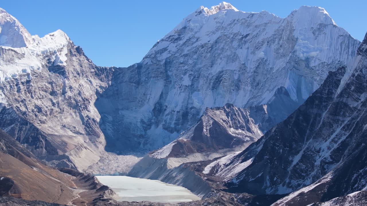 Inquadratura aerea in parallax con drone che riprende il lago glaciale Imja sotto le montagne himalayane innevate nella regione dell'Everest in Nepal, rivelando un drammatico terreno alpino.