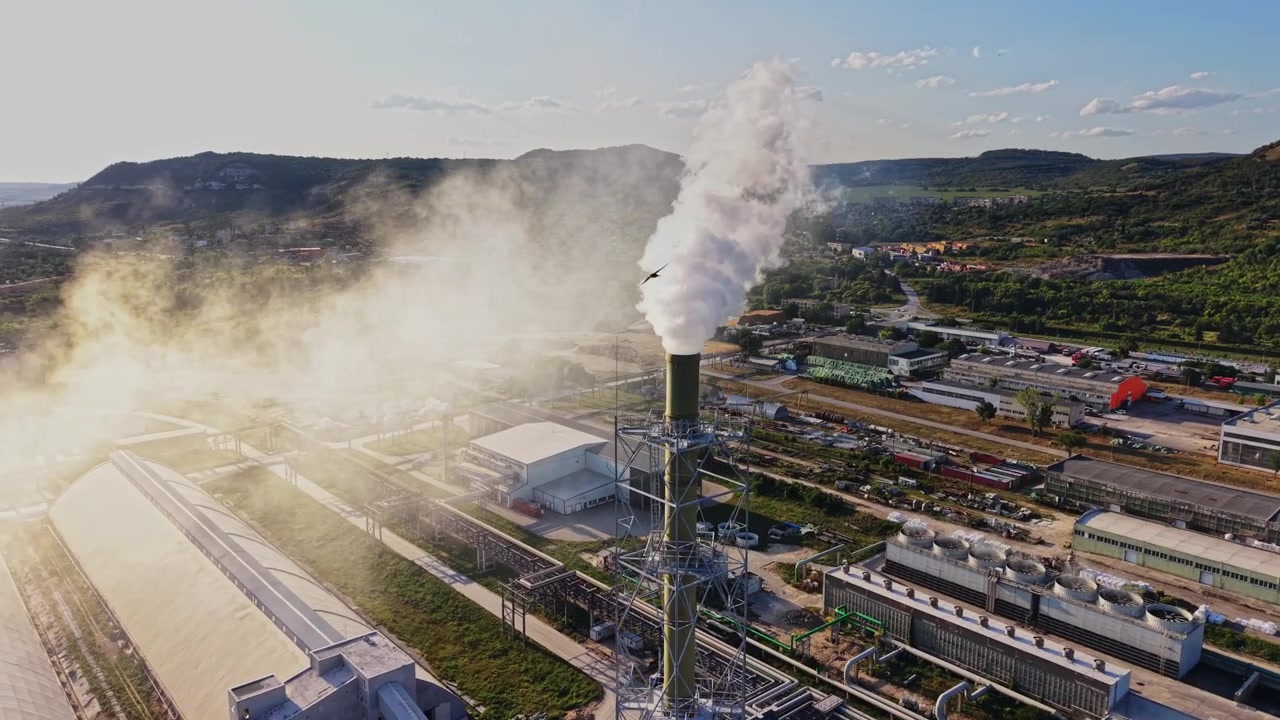 Fumo che sale da una ciminiera di fabbrica in un'area industriale durante il giorno