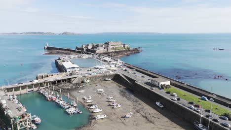 Flight-over-fishermans-marina,model-yacht-pond,yacht-club-and-boatyard-to-Castle-Cornet-on-sunny-day,historic-castle-in-St-Peter-Port-Guernsey-with-calm-clear-sea-and-views-over-Jethou,Herm-and-Sark