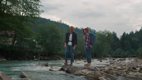couple standing on rocky shore of river. tourists touching water in river