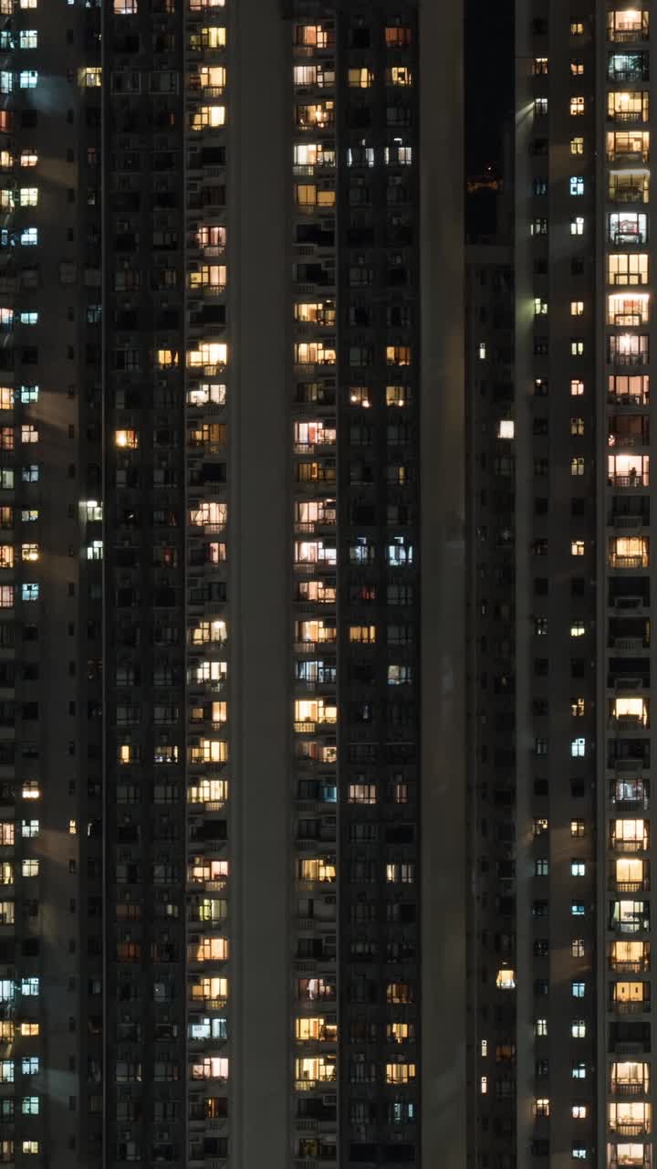 Vista vertical de um edifício residencial alto com janelas iluminadas à noite.