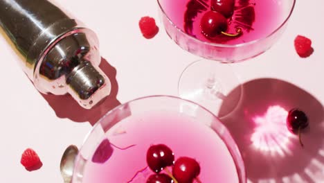 close up of drinks with cherries and shaker on white background