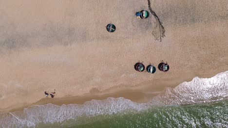 drone flies bird’s-eye facing down from the sandy beach to the sea, revealing fisherman buckets in the sand and the shoreline in a peaceful coastal scene.