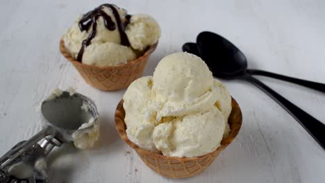 jarabe de chocolate que se vierte sobre bolas de helado de vainilla en un tazón de cono de gofre cubierto con una pieza de caramelo de colores