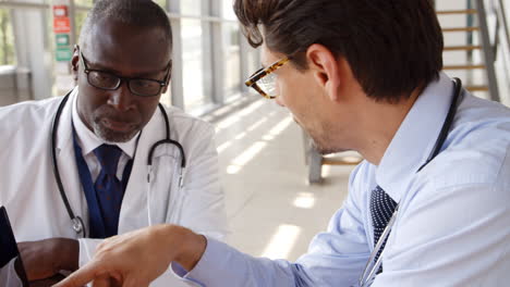 Two-Male-Doctors-Having-Meeting-Sitting-Around-Table-In-Hospital