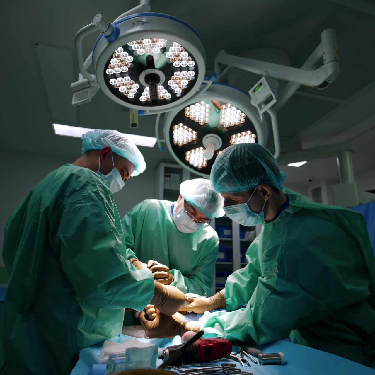 Surgeons perform operation on the injured foot. Assistant holds the patient's foot and surgeons use the tools and devices
