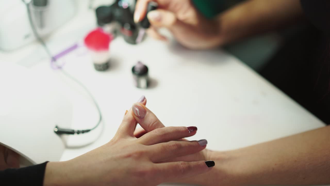 master of manicure is painting a woman's nail with a brush in a pink color in a beauty salon at the table. Manicure of hands
