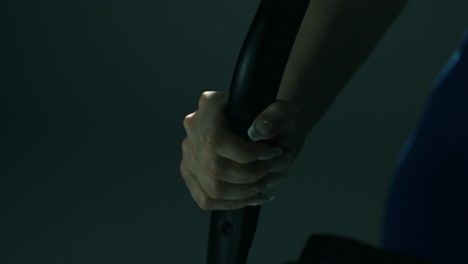 macro closeup of a fit woman’s hands gripping stationary bike handlebars, showing long nails and firm control, as the camera glides from one hand to the other in dramatic indoor studio lighting
