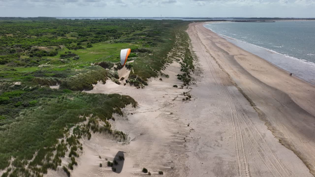 Drone crane motion of paraglider soaring above lush Dutch seaside sand dunes