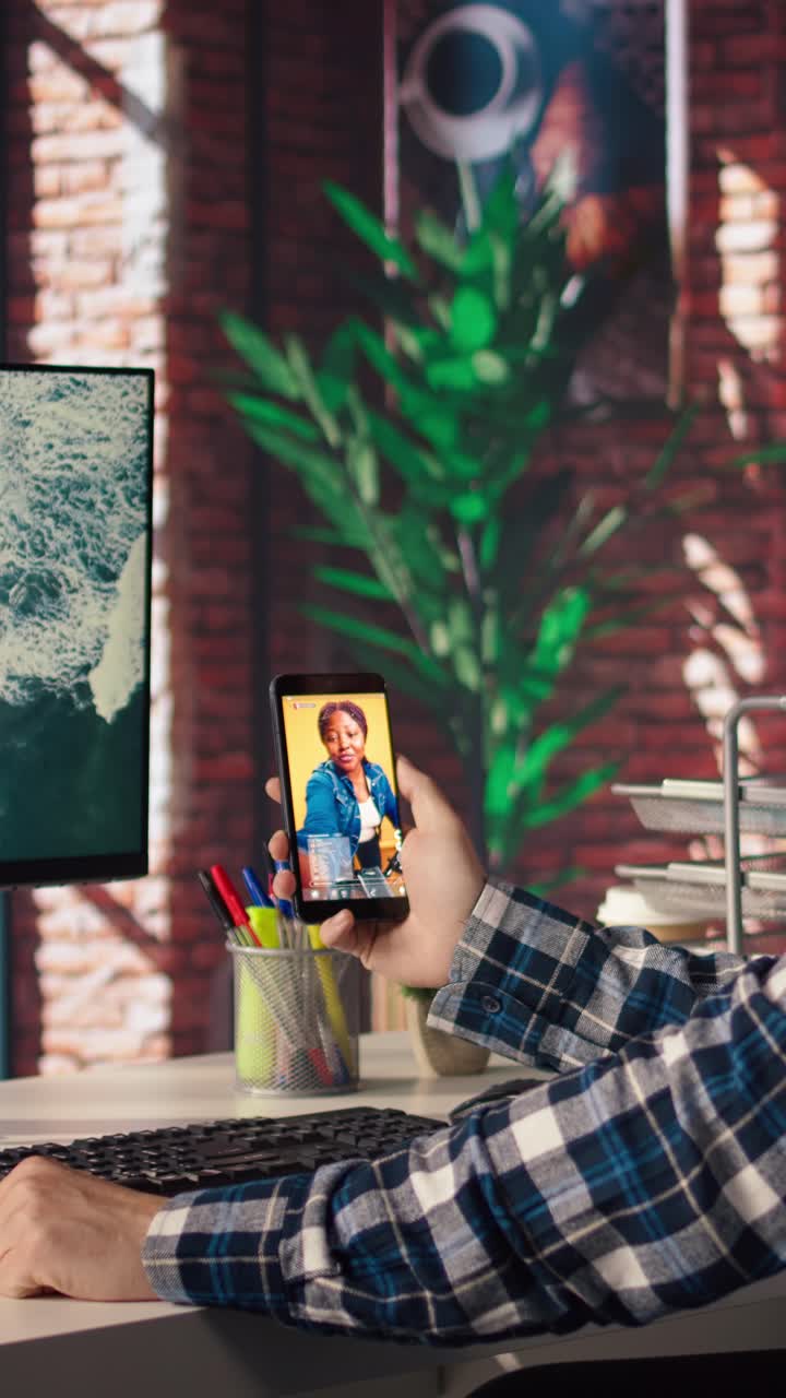 Vertical video Man using phone, having PC monitor idle in front of him showing screensaver