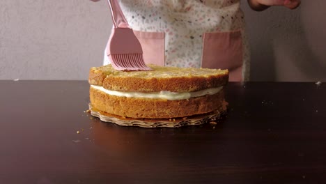 Latin-woman-wearing-an-apron-preparing-cooking-baking-a-cake-spreading-milk-with-a-pink-silicon-brush