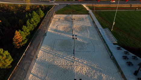 aerial tilt up reveals outdoor sand volleyball courts during golden hour light