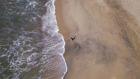 a woman walks along a beach as seen from an overhead aerial drone