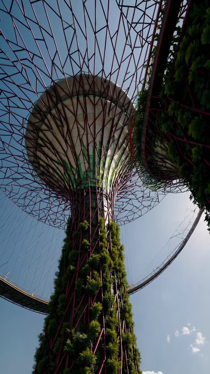 Blick aus niedriger Perspektive auf einen futuristischen, pflanzenbewachsenen Turm vor hellem Himmel.