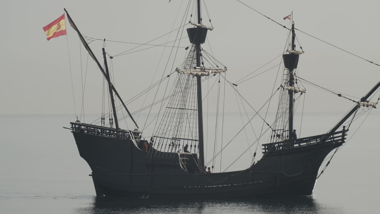 ferdinand magellan nao victoria carrack 보트 복제품과 스페인 국기가 있는 보트 복제품은 슬로우 모션 60fps로 잔잔한 바다 쪽에서 일출 시 지중해에서 항해합니다.