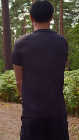 vertical video rear view shot of man warming up and stretching arms before work out exercising running through forest 2