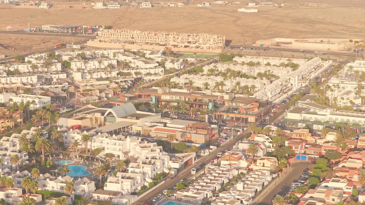 Warm sunlight illuminating white buildings, swimming pools, palm trees and streets of a coastal tourist resort in Playa del Medio, Canary Islands, Spain, creating a inviting summer holiday atmosphere