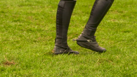 person in riding boots walking through the grass at an equestrian competition