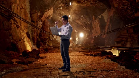 Full Body Side View Of An Asian Male Professional Worker Standing With His Laptop In Underground Mine Tunnel, He Raises His Fist Up With Screaming Goal After Typed On The Laptop