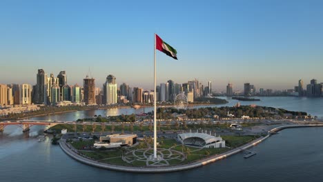 vista aérea de la bandera de los emiratos árabes unidos ondeando en el aire, el cielo azul de fondo, el símbolo nacional de los emiratos árabes unidos sobre la isla de la bandera de sharjah, emiratos árabes unidos, video 4k