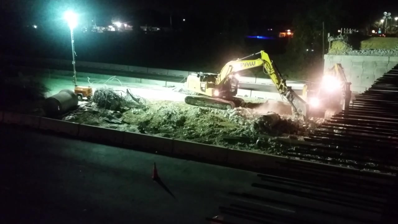Coppia di escavatori al lavoro di notte in un cantiere stradale nel mezzo di un'autostrada trafficata