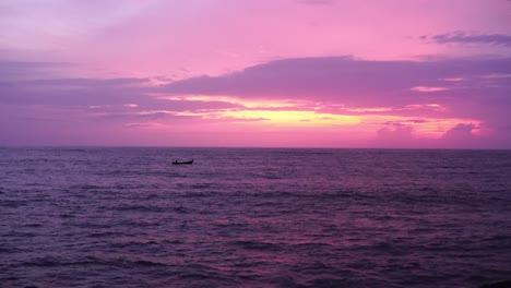 panoramic view of long tail fishing boat passing the ocean after sunset with beautiful pink and reddish sky in the ocean