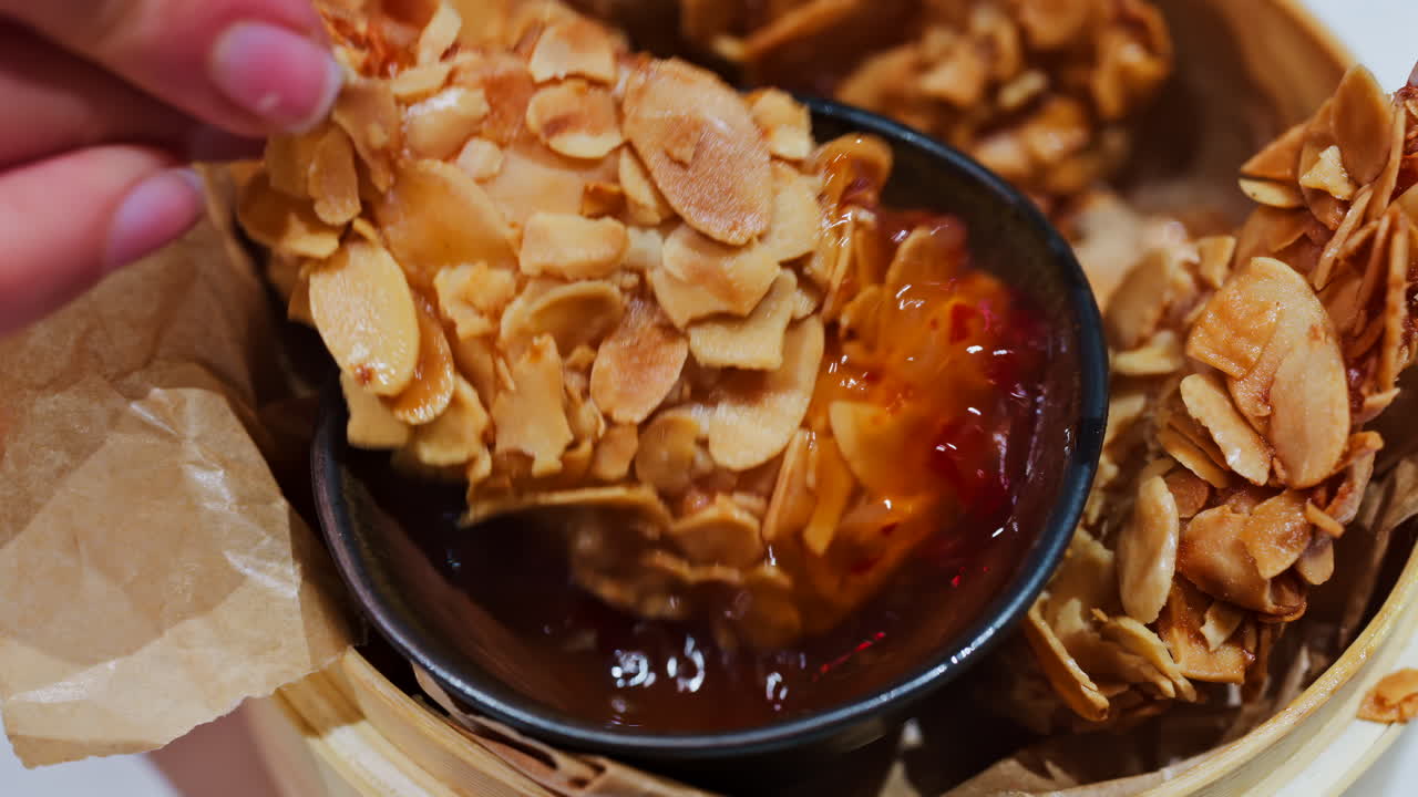 Close up of a woman dipping a crispy, almond-coated fried food into a red sauce