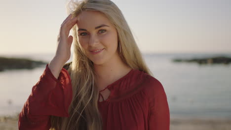 Primer-Plano-Retrato-De-Una-Hermosa-Joven-Rubia-En-La-Playa-Sonriendo-Coqueta-Pasa-La-Mano-Por-El-Cabello-Sintiéndose-Segura