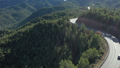 BMW-driving-Montserrat-mountain-road,-aerial-view-reveal-lush-scenic-Catalonia-woodland-mountain-valleys