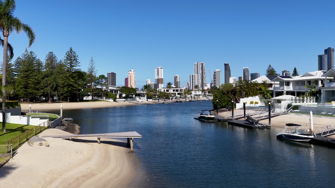 Daytime camera pan reveals luxury waterfront homes, sandy beach, boats, and city skyline