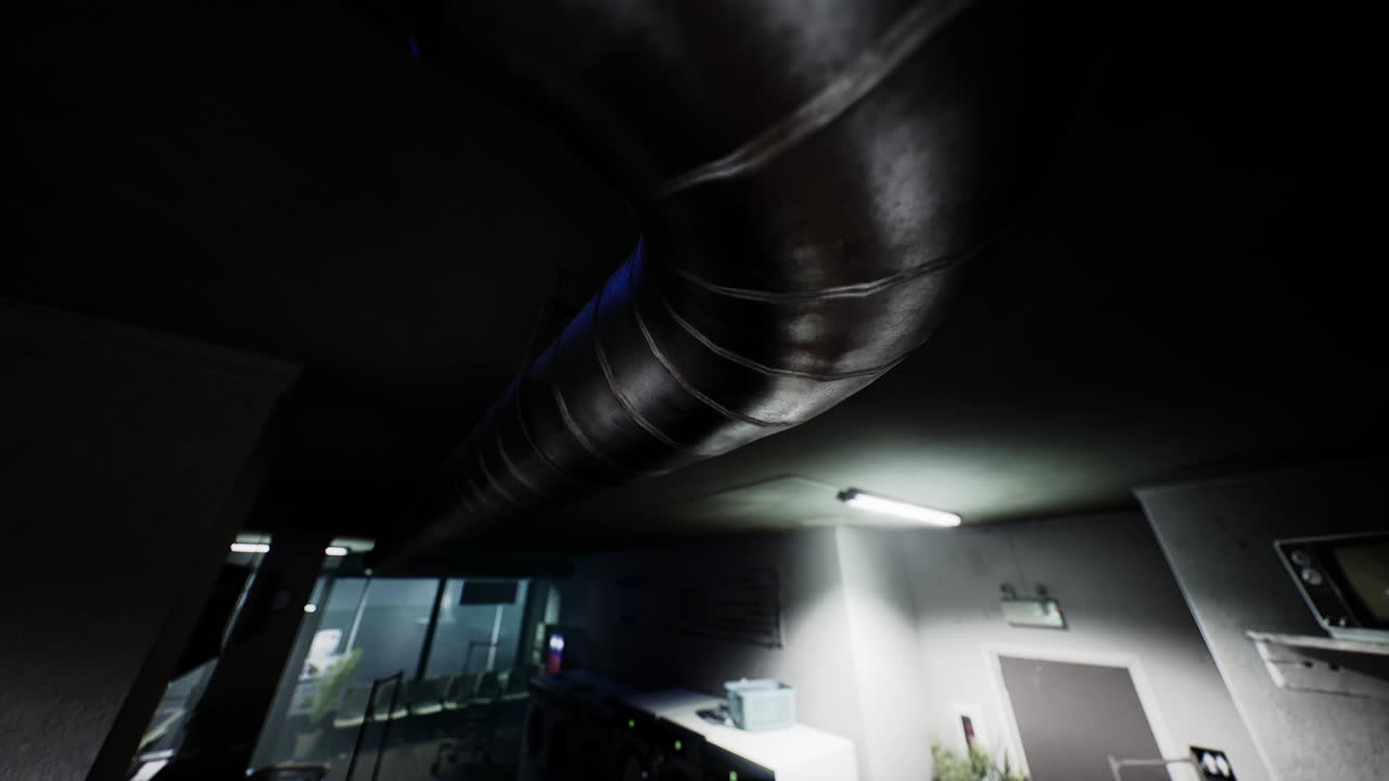 형광등이 있는 어두운 방에서 천장을 통과하는 금속 파이프의 클로즈업입니다.