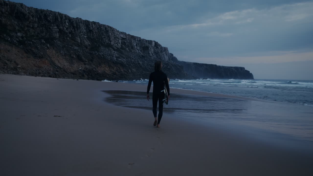 un surfista caminando por una playa al atardecer