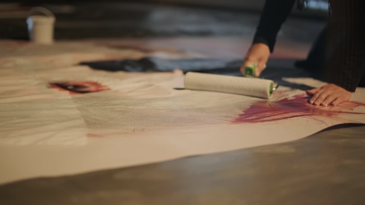 mujer creativa dibuja en el lienzo grande con un rodillo blanco de pintura en el suelo en el estudio de arte