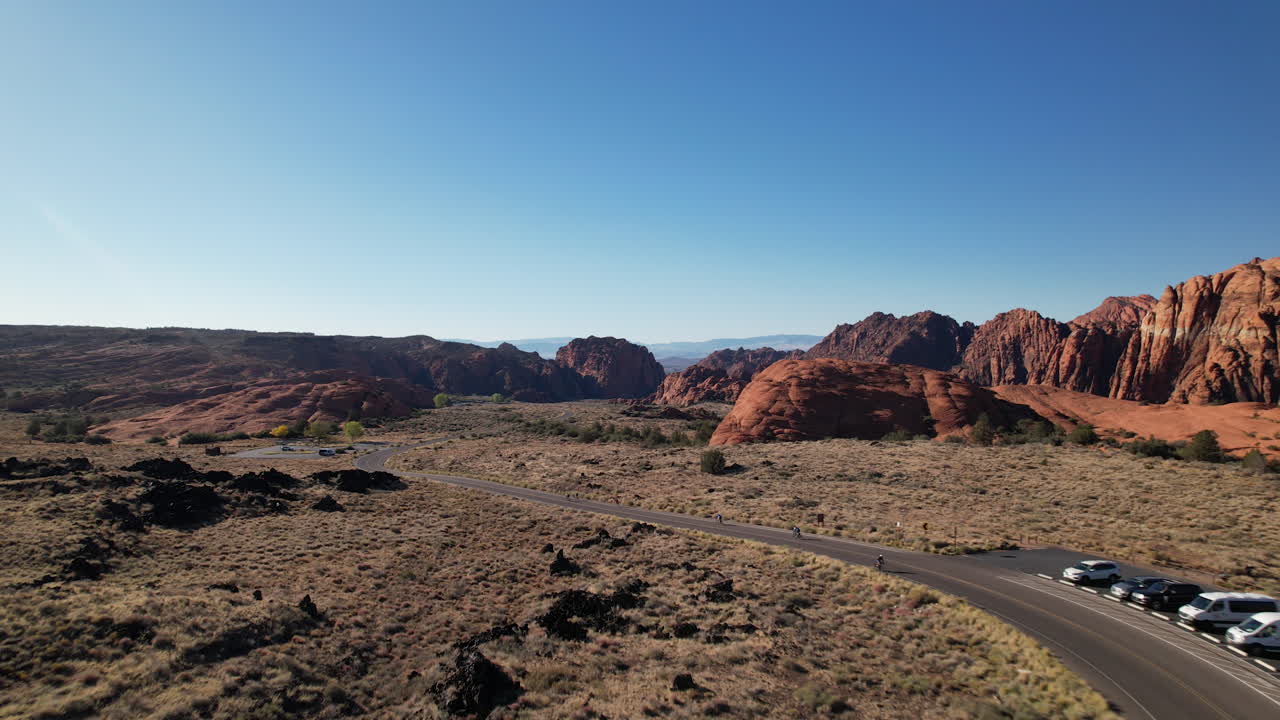 Drone shot tracking triathletes along a winding road through Snow Canyon, Utah, highlighting the stunning red rock formations, desert landscape, and natural beauty of the canyon.
