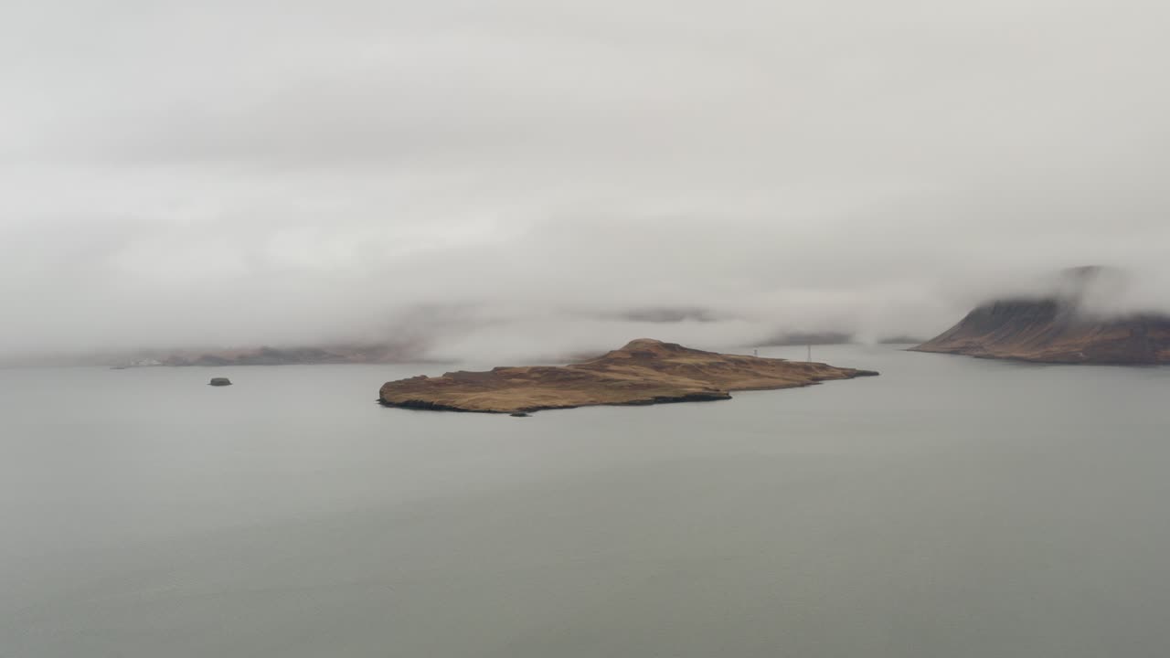Nuvole che si addensano su un'isola isolata nella tranquilla e nebbiosa baia di Hvalfjörður, in Islanda, circondata da acque calme e da una suggestiva nebbia bassa sotto un cielo nuvoloso