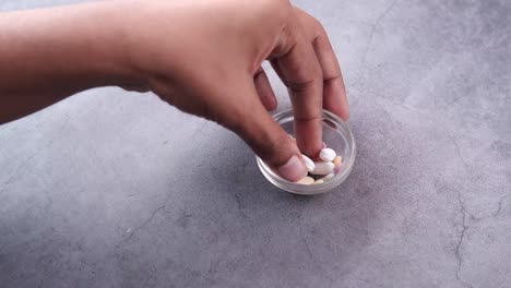 hand holding a small glass bowl with various pills